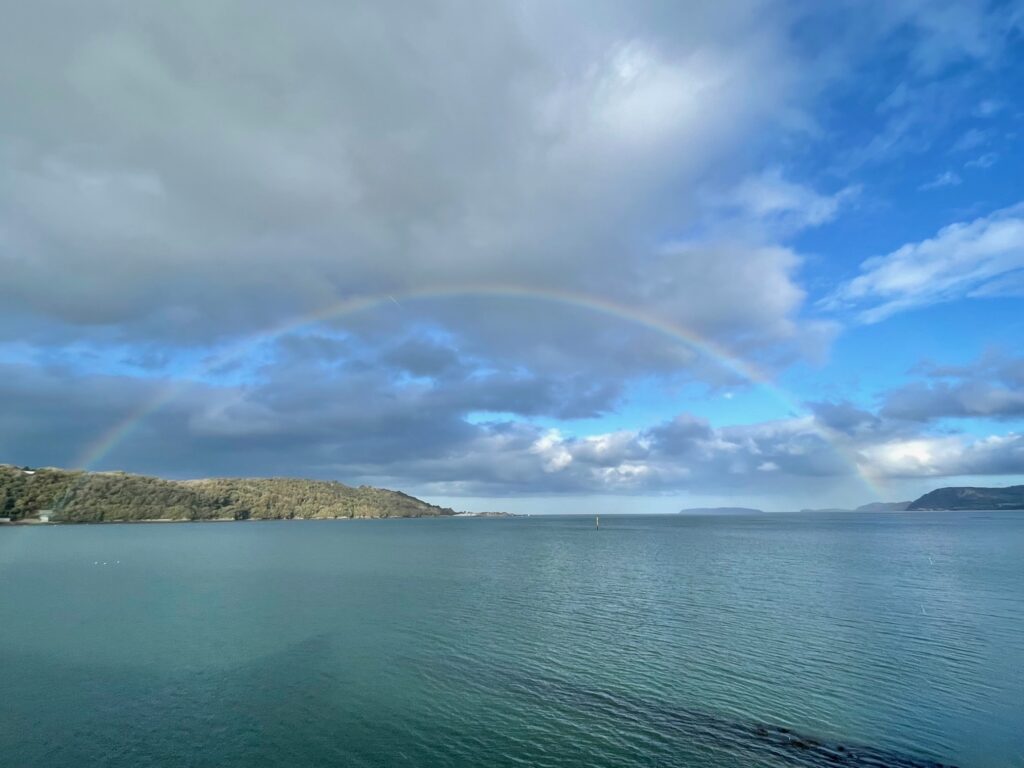 Rainbow against a partly cloudy sky over a stretch of sea