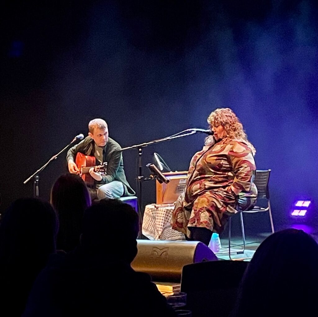 A man playing guitar and a woman singing on stage.