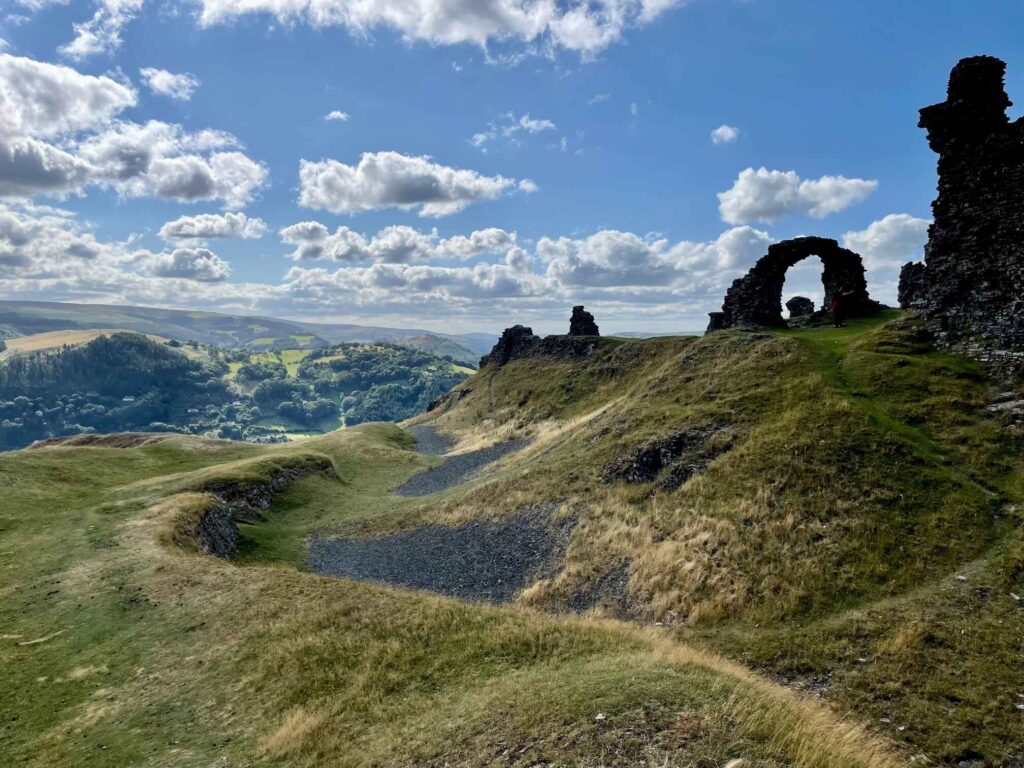 Ruins of a medieval Welsh castle with puffy white clouds against a bright blue sky. 